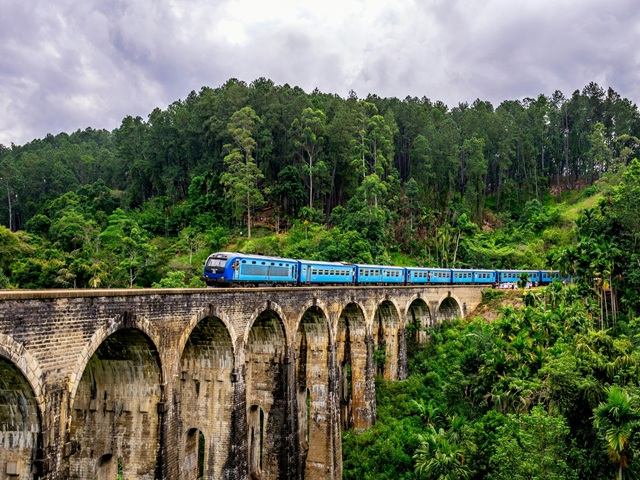 Colorful train passing over the Nine Arch Bridge in Ella surrounded by lush green jungle