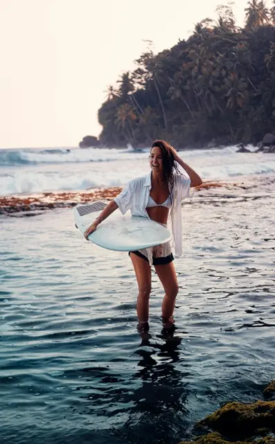 Young woman holding a surfboard on the shore of Mirissa Beach