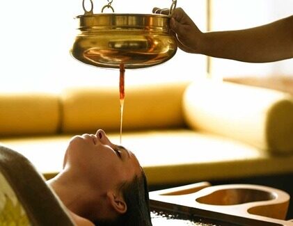 Woman undergoing Shirodhara with herbal oil dripping onto forehead
