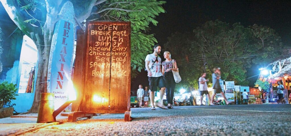 Couple walking through Arugam Bay town at night visiting cafés