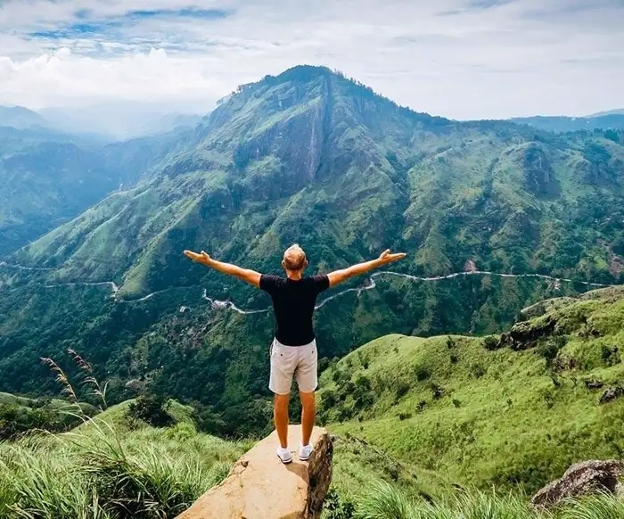 Man standing with open arms and looking over Ella Gap from Little Adam's Peak in Sri Lanka